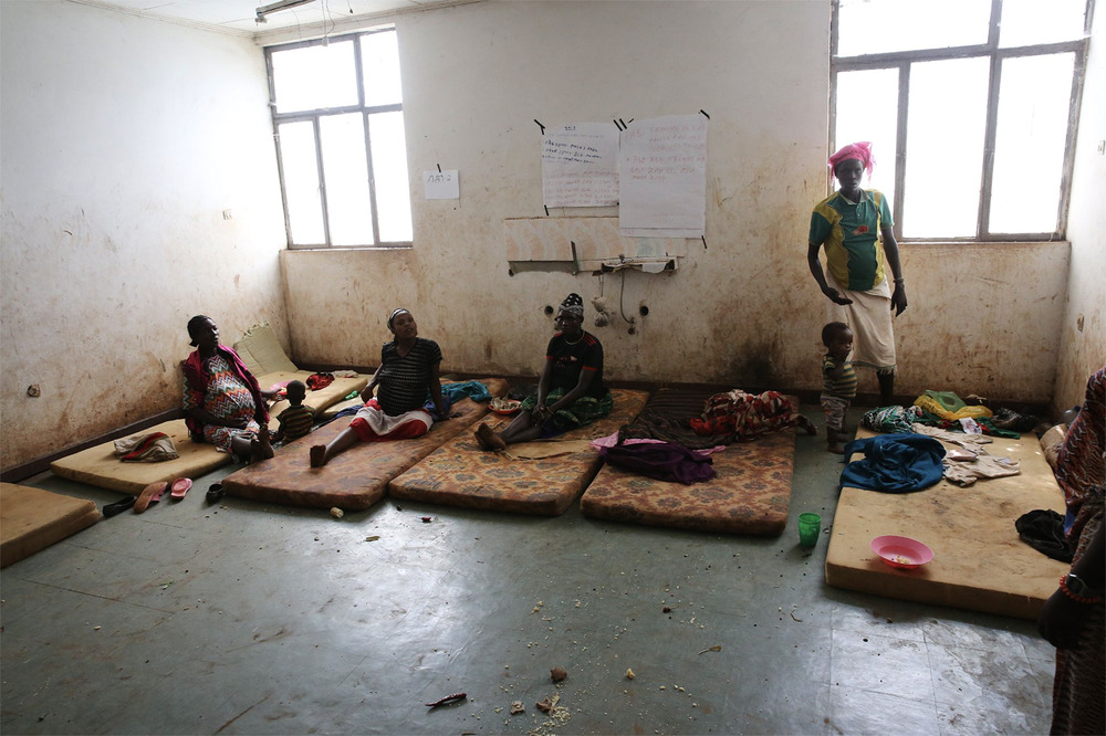 Women sit on dingy mattresses in squalid room