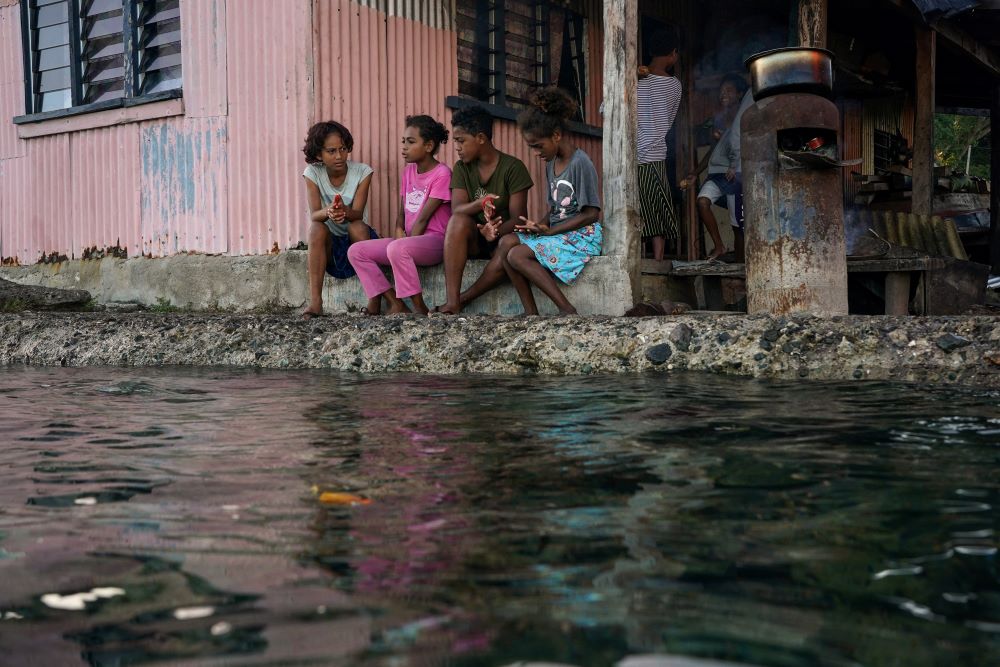 Village children pass the time in front of a home next to a flooding sea wall at high tide in Serua Village, Fiji, July 15, 2022. (CNS/Reuters/Loren Elliott)