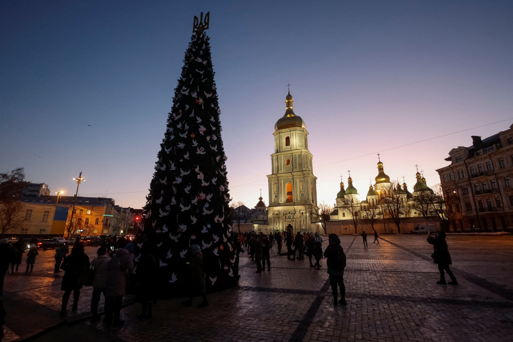 A tall Christmas tree stands in a plaza in front of a church at twilight