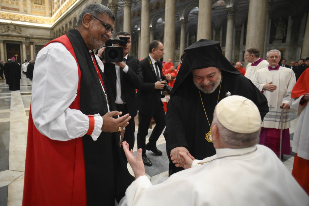 A man wearing a koukoulion, an Orthodox headdress, shakes Pop Francis' hand, as a Brown man with Black and red vestments stands next to him.