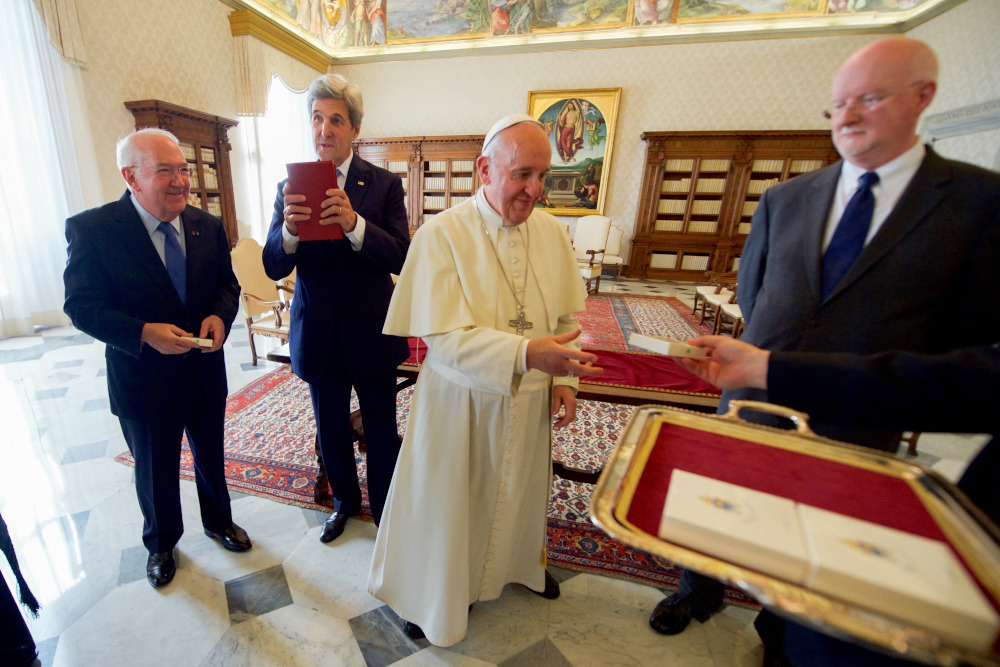 U.S. Special Representative for Religion and Global Affairs Shaun Casey looks on as Pope Francis prepares to present him with a Papal medallion on December 2, 2016, following a one-on-one meeting with U.S. Secretary of State John Kerry in the Papal Apartments at the Vatican in Vatican City. (Wikimedia Commons/State Department)