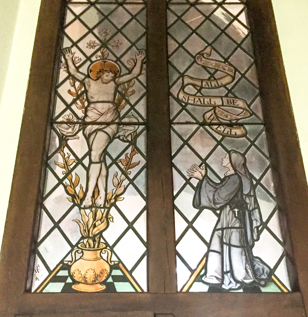 A stained glass window shows a woman kneeling in supplication before Jesus on the cross