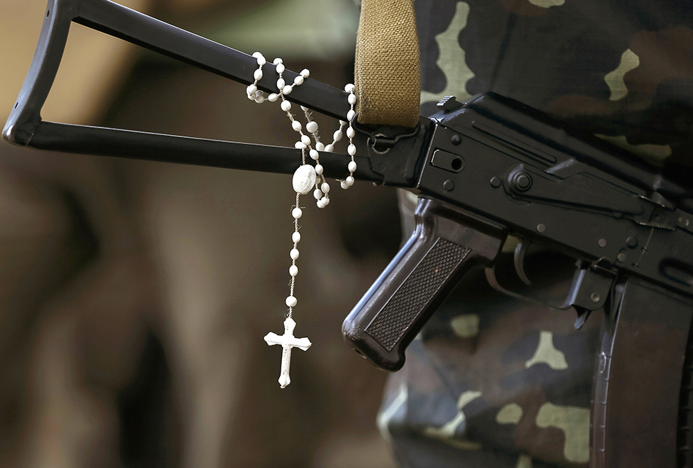 A rosary hangs from a machine gun in an undated file photo as Ukrainian soldiers stand at their positions near the Ukrainian town of Pervomaysk. (OSV News/Reuters/Gleb Garanich)