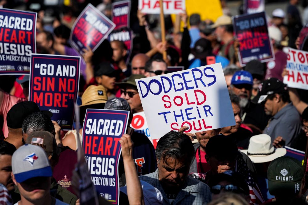 Protesters hold signs that read "Dodgers sold their soul"