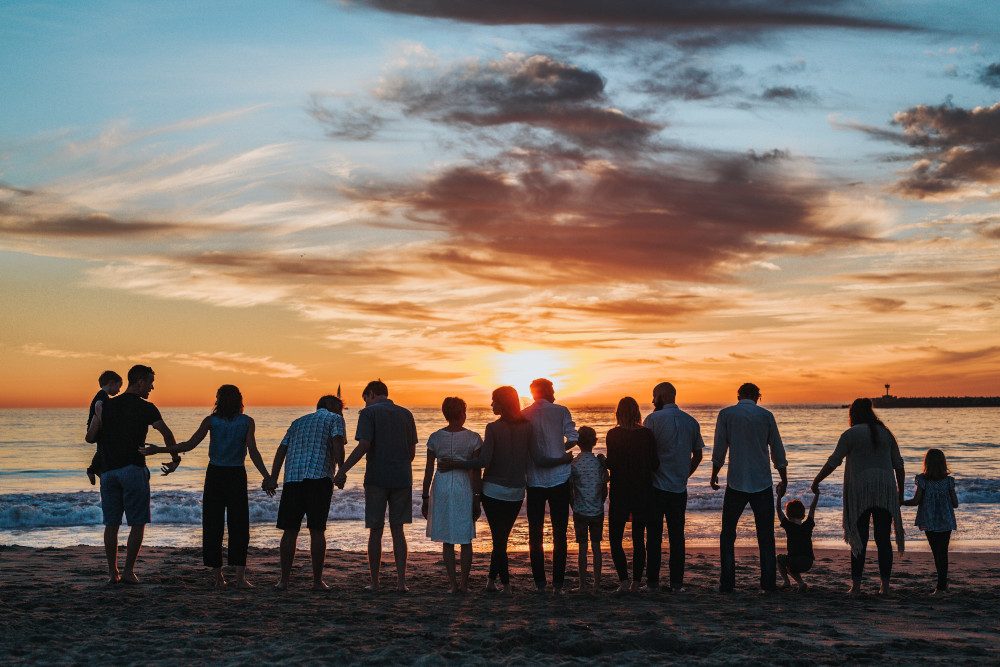 A photo taken at sunset of a family gathered by the shore (Unsplash/Tyler Nix)