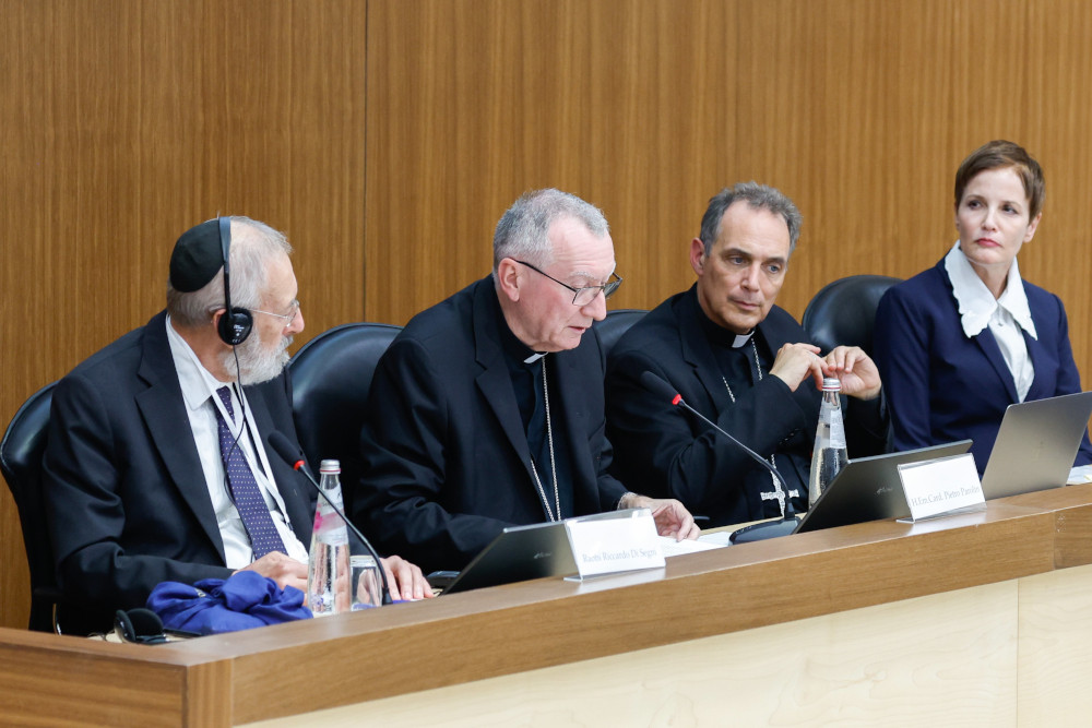A man wearing a kippah sits next to two men wearing Catholic clerical shirts and a woman in Western business attire