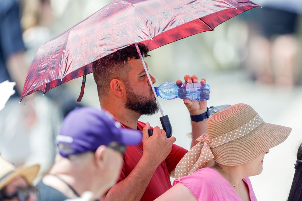 A man cools off from the heat under an umbrella as he drinks water while visitors wait for the start of Pope Francis' Angelus prayer in St. Peter's Square at the Vatican July 9, 2023. (CNS photo/Lola Gomez)