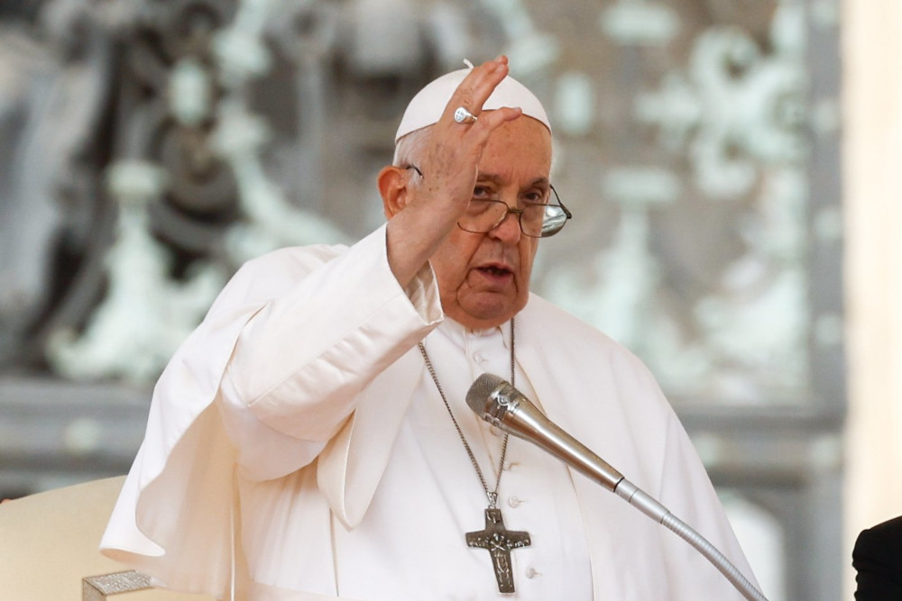 Pope Francis raises his right hand as he speaks into a microphone