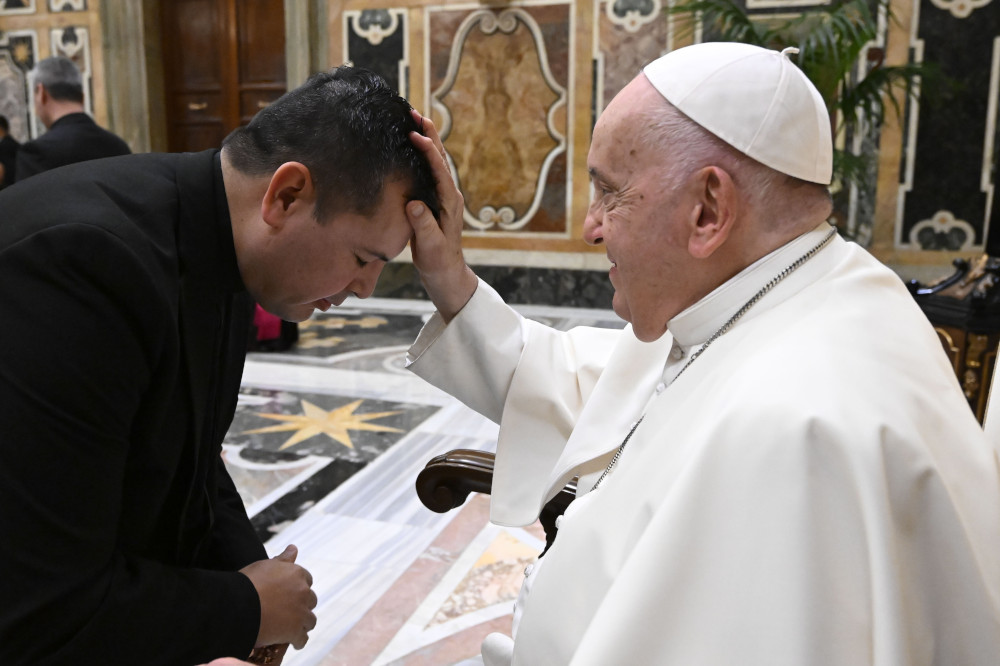 Pope Francis places his hand on the head of a black-haired priests who bows before him