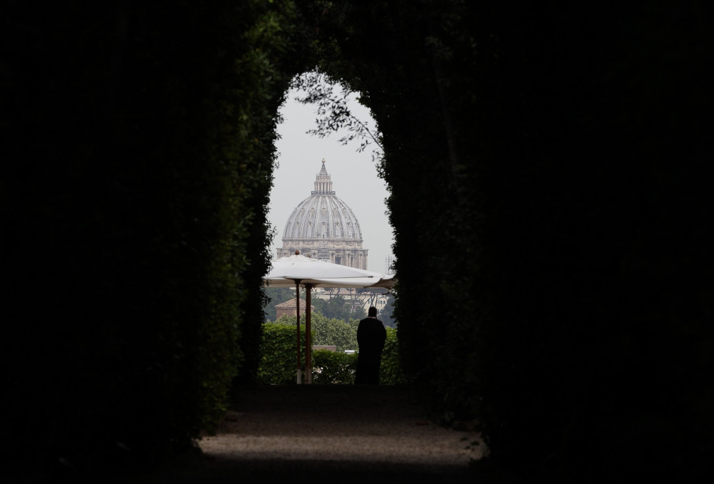 The dome of St. Peter's Basilica is visible through an arched window in a stone wall