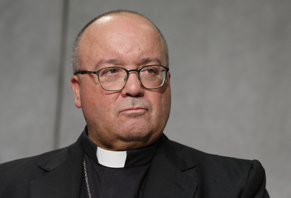A white man with a buzz cut wears glasses, a clerical collar and a pectoral cross