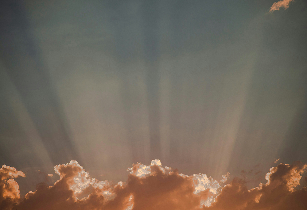 A photo illustration shows light emerging from underneath clouds in the sky. (Unsplash/Ben Vaughn)