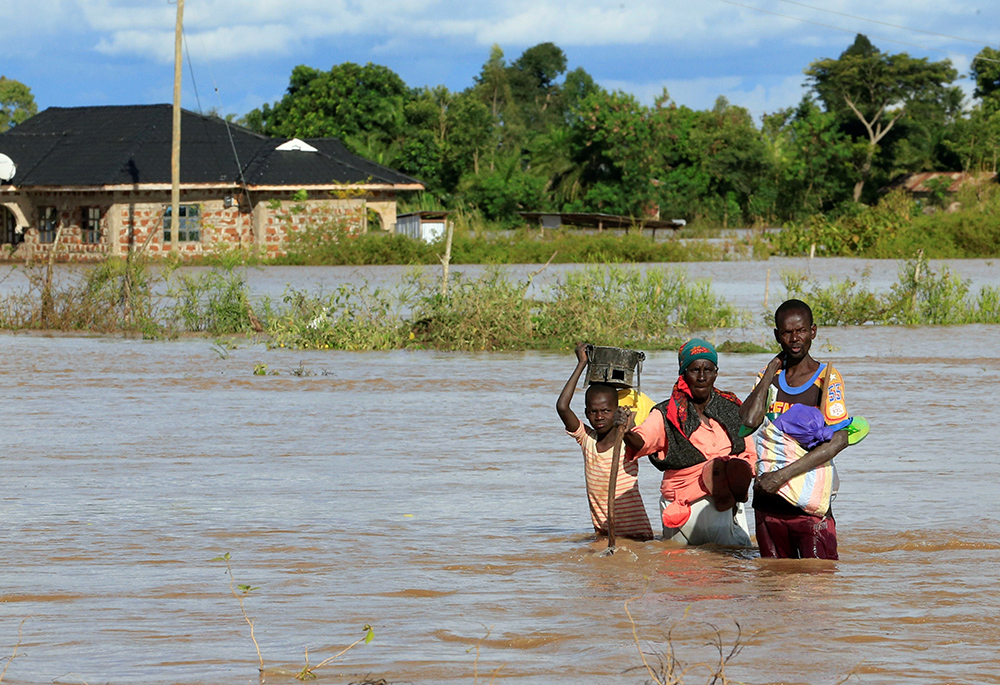 A boy and young man help a woman wade through floodwaters May 3, 2020, in Busia, Kenya. With more than 1,000 acres of western Kenya's Maragoli Forest degraded, surrounding communities are subjected to climate impacts like recurrent drought, hunger and flooding. (CNS/Reuters/Thomas Mukoya)