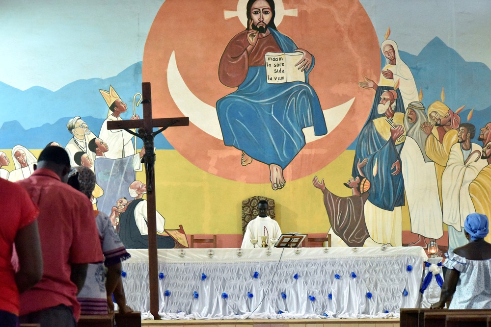 Worshippers in Burkina Faso church with vibrant mural behind altar