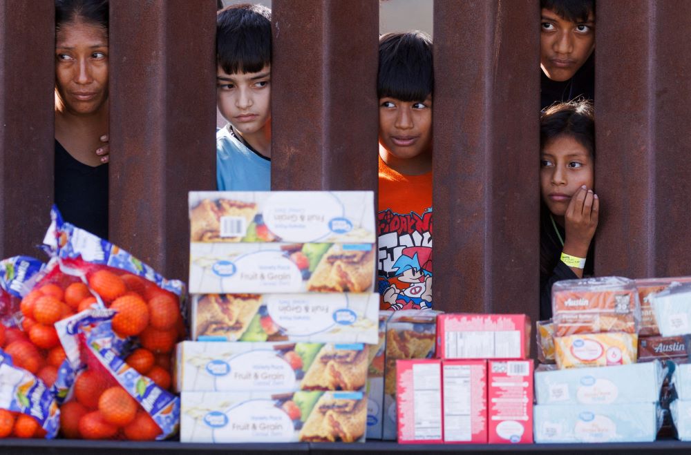 Migrants look through the border fence Sept.12, 2023, toward food brought by aid workers after gathering between the primary and secondary border fences at the U.S.-Mexico border