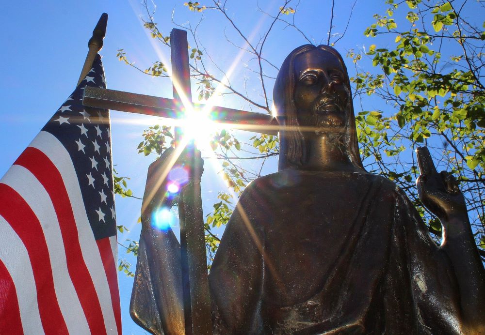 Sun shines through a statue of Christ on a grave marker alongside an American flag at St. Mary Catholic Cemetery in Appleton, Wis.