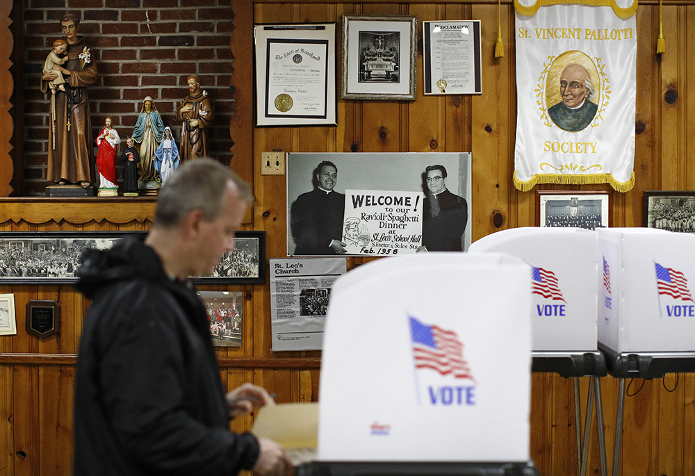Religious artwork and vintage photographs adorn a wall behind a voter as he completes his ballot at a polling place inside St. Leo the Great Roman Catholic Church, Nov. 6, 2018, in Baltimore. (AP photo/Patrick Semansky)