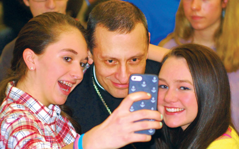 Bridgeport, Conn., Bishop Frank Caggiano snaps a selfie with two teens at a town hall forum in February. (Fairfield County Catholic/Amy Mortensen)