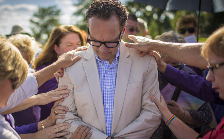 Parishioners place their hands on Colin Collette to pray Sept. 7 during a vigil to support him outside Holy Family Parish in Inverness, Ill. Collette, a music minister, was fired from Holy Family after his engagement to a man became known. (Chicago Tribune/Brian Cassella)