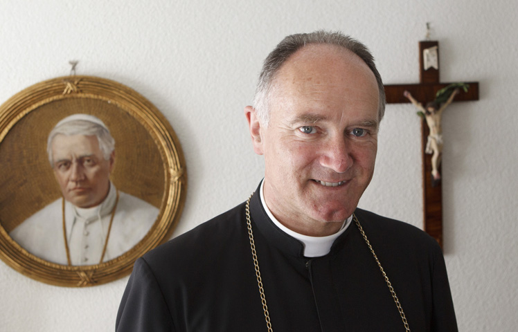 Bishop Bernard Fellay, superior of the Society of St. Pius X, is pictured near an image of St. Pius X at the society's headquarters in Menzingen, Switzerland, May 11, 2012. (CNS/Paul Haring)