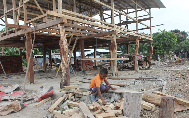 A boy sorts through pieces of wood outside a house being rebuilt following an April earthquake in the village of Bigua, Ecuador July 27. (CNS photo/Barbara Fraser)