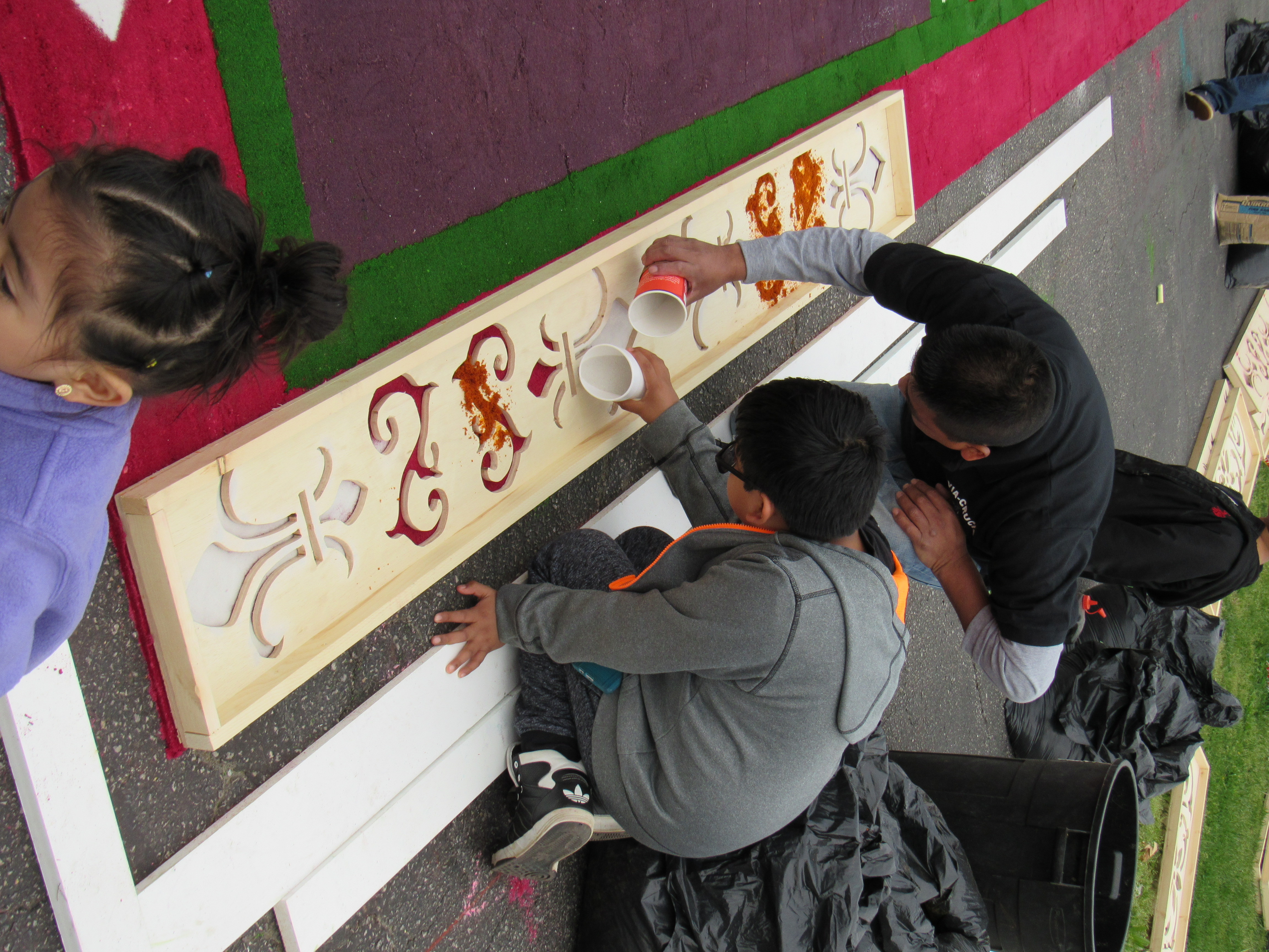 Nearing completion, workers pour sawdust into forms for the border of the carpet.
