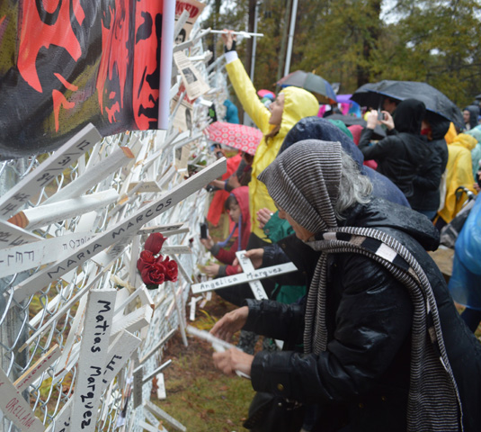 Members of the 25th annual SOA Watch vigil place white crosses bearing names of Latin American martyrs into the fence surrounding the Western Hemisphere Institute for Security Cooperation on Sunday in Columbus, Ga. (Veronica O'Neill)