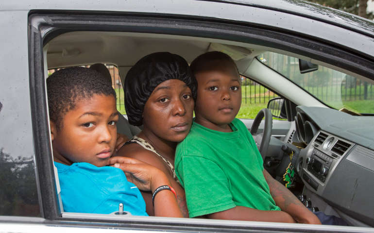 Katrina Robinson and her two sons, David Collins, 11, and Dabion Collins, 7, pose for a photo in their family car in Detroit Aug. 7. Since May, on the nights when they are unable to crash with family or friends, the family car is the only shelter Robinson and her two young sons have. (CNS photo/Jim West)