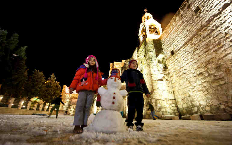 Children pose with a snowman outside the Church of the Nativity in the West Bank town of Bethlehem Jan. 9 during a rare cold spell. (CNS photo/Marcin Mazur, Bishops' Conference of England and Wales) 