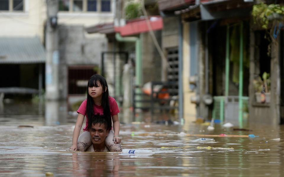 A man carries a child on his shoulders through a flooded street in Manila, Philippines, following Typhoon Vamco. (CNS/Reuters/Lisa Marie David)