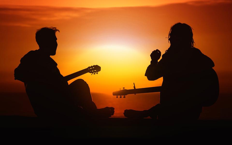 Two musicians play guitar outside, appearing in silhouette against a sunset. (Pixabay/Gerd Altmann)