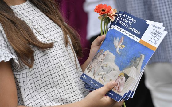 A young woman holds flowers and copies of Pope Francis' message for the first World Day for Grandparents and the Elderly. At the end of a Mass July 25 in St. Peter's Basilica at the Vatican, young people handed out flowers and copies of the message.