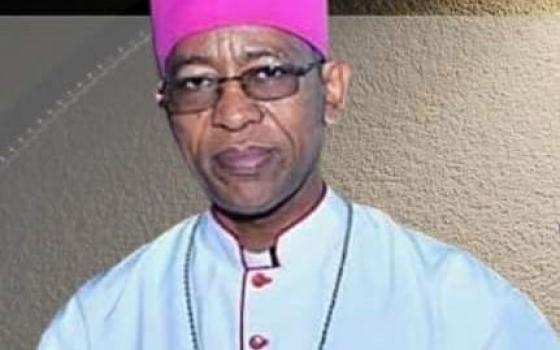 A Black man with glasses and a bishop's clothing looks at the camera