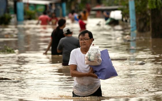 A man carries his belongings through floodwaters Sept. 26, 2022, after Typhoon Noru hit Bulakan, Philippines. Noru left a trail of destruction in northern Philippine provinces and was headed toward Vietnam. (CNS photo/Eloisa Lopez, Reuters)