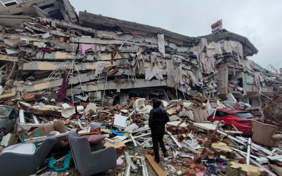 A person stands in front of a massive collapsed building