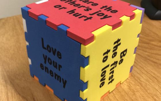 A cube in primary colors has phrases like, "Be the first to love," "Share the other's joy or hurt," and "Love your enemy."