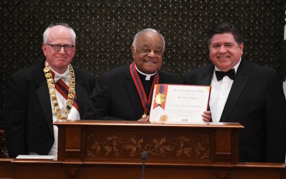 Cardinal Wilton Gregory, wearing a cassock and medal, holds a certificate and stands between two other men
