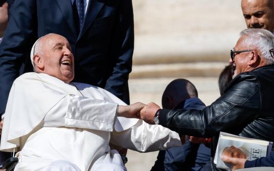 Pope Francis throws head back, laughing and gripping hand of guest