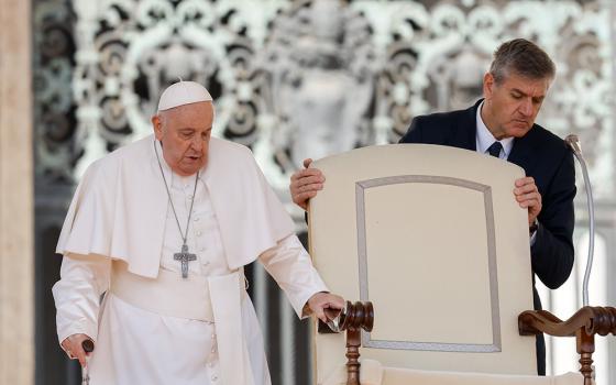 Pope Francis, walking with a cane, reaches his chair held by his aide, Sandro Mariotti, as he arrives for his weekly general audience in St. Peter's Square at the Vatican March 20, 2024. (CNS/Lola Gomez)