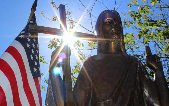 Sun shines through a statue of Christ on a grave marker alongside an American flag at St. Mary Catholic Cemetery in Appleton, Wis.