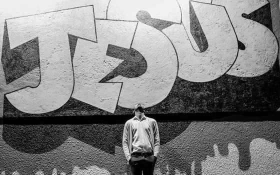 Man standing looking up in front of graffiti style lettering "Jesus"