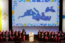 Pope sits with bishops in front of a large map of the Mediterranean region.