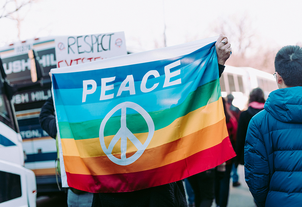 In this photo illustration, a protester holds up a rainbow-colored flag that displays the word 