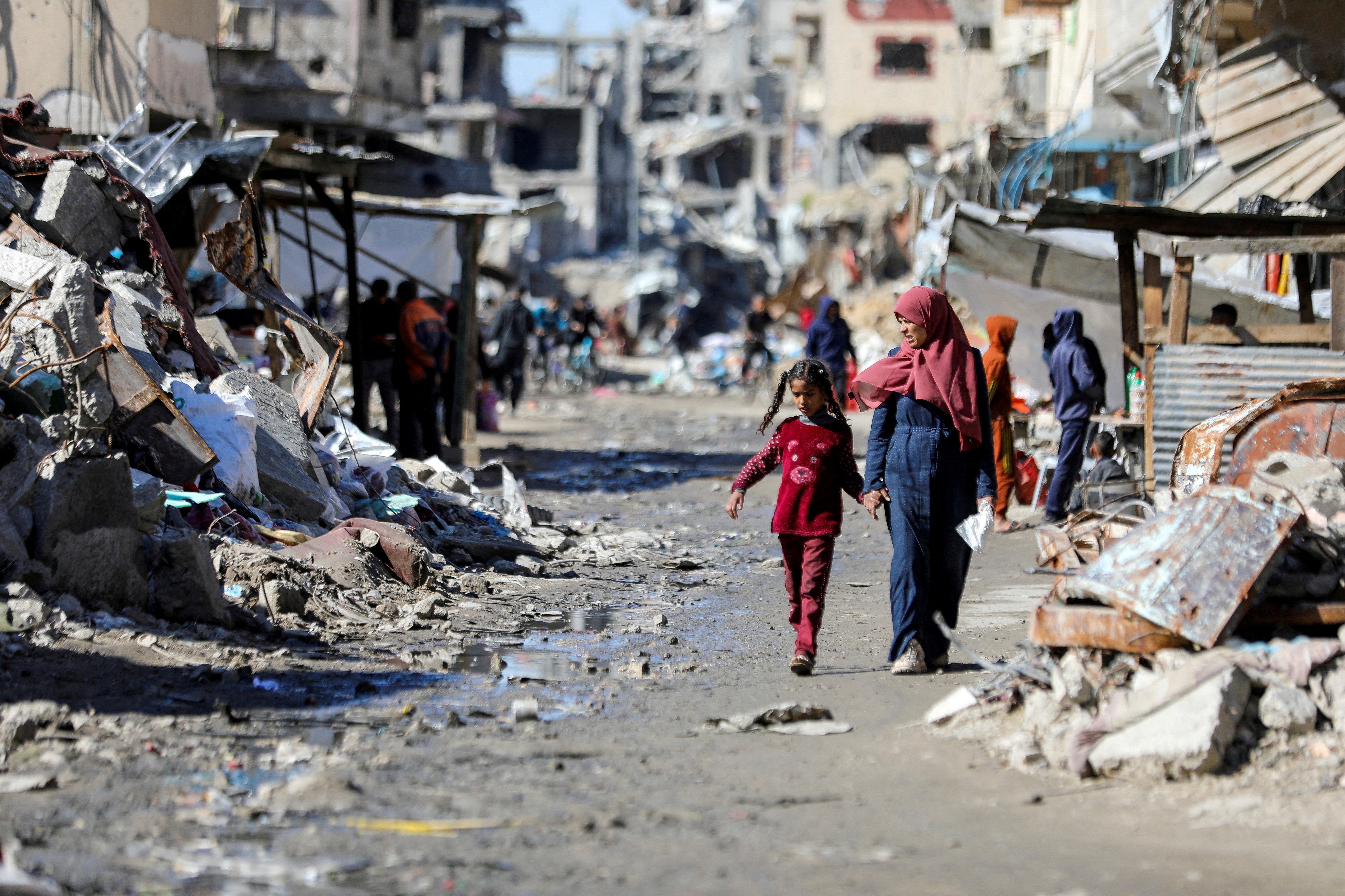 Women and young girl walk hand in hand through ruins. 