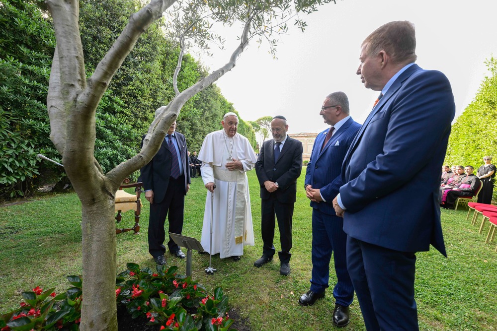 Pope and dignitaries stand around olive tree in garden while speaking