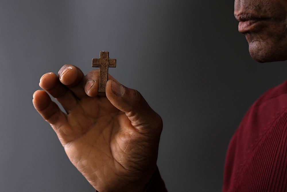 A black man holds in front of him a small wooden cross (Dreamstime/Derektenhue)
