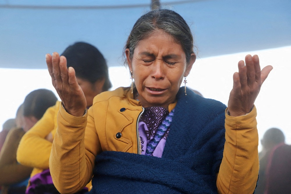 Woman holds hands up, and bows head in prayer. 