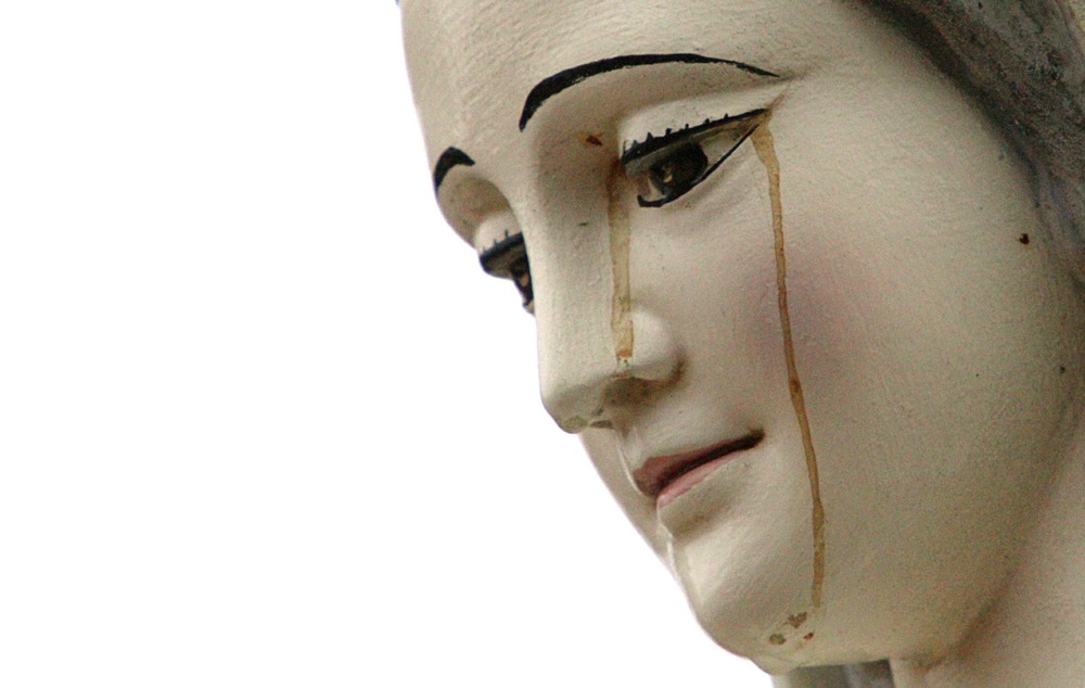 Marian statue up close, brownish liquid seeps down face. 