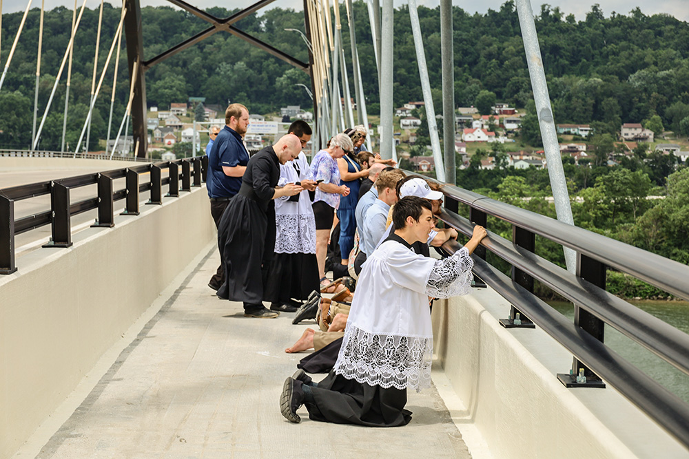 Priests, seminarians and faithful from the Diocese of Steubenville, Ohio, kneel and pray the rosary on the Wellsburg Bridge in West Virginia as a sternwheeler carrying the Eucharist passes below on the Ohio River. (OSV News/The Catholic Spirit/Colleen Rowan)