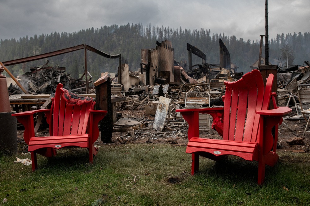 Melted lawn chairs shown in front of incinerated house and smokey, charred landscape. 